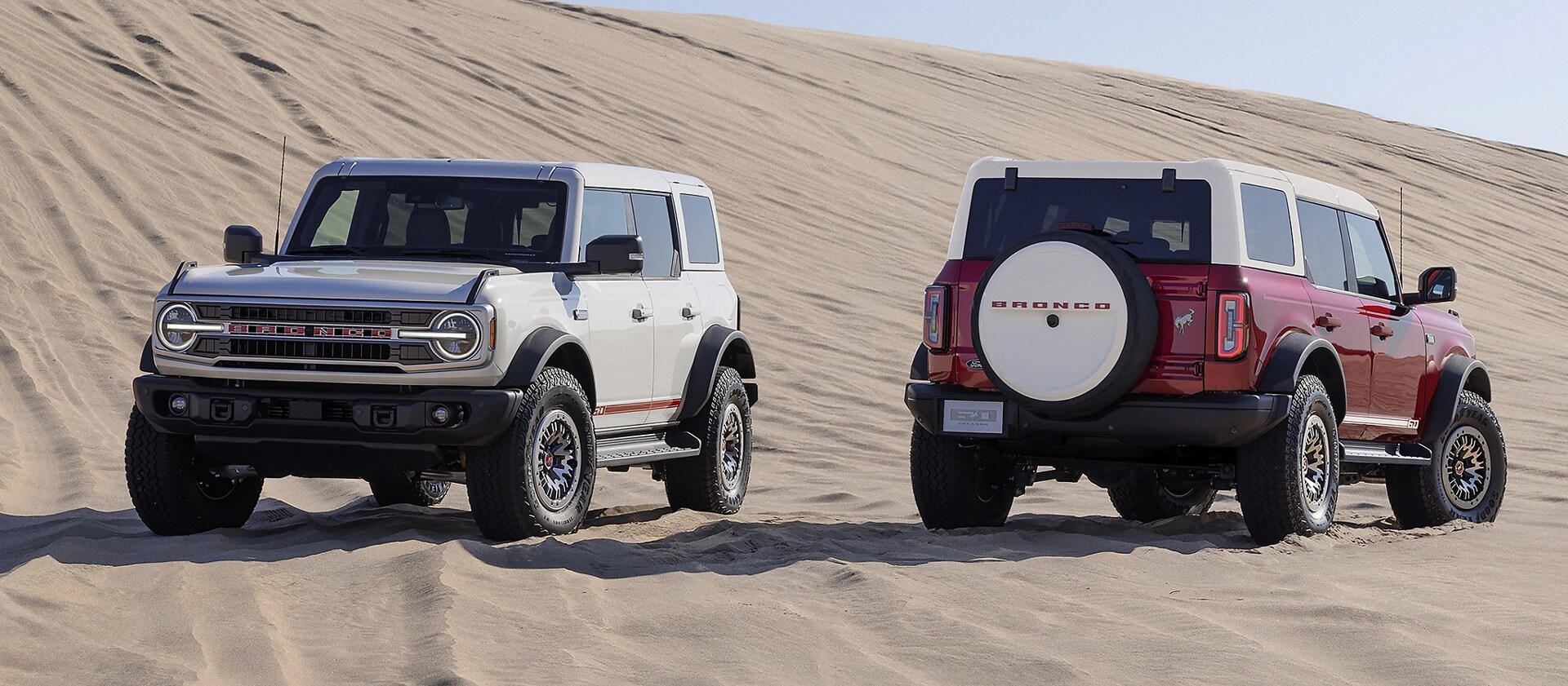 Two 2026 Ford Bronco® Outer Banks® SUVs with the available 60th Anniversary Package, parked on a sand dune